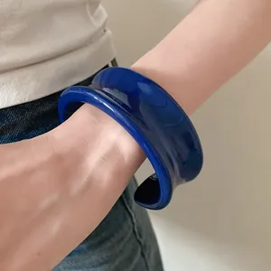 Vista dettagliata di un bracciale rigido aperto in resina blu reale indossato sul polso.