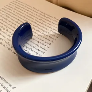 Primo piano di un bracciale rigido in resina blu scuro lucida su una pagina di libro.