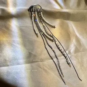 Elegant jellyfish brooch with long pearl and rhinestone tassels on silk background.