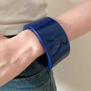 Dettaglio di un ampio bracciale rigido in resina blu scuro indossato sul polso