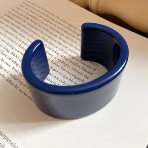 Dettaglio di un bracciale a fascia in resina blu scuro posizionato su un libro aperto.