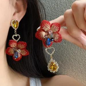 Primo piano di orecchini asimmetrici a fiore rosso con cristalli gialli a goccia.