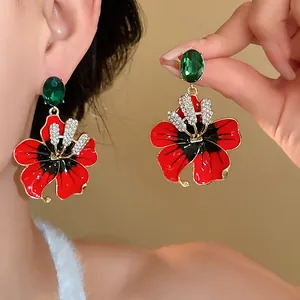 Vista ravvicinata di eleganti orecchini a fiore rossi con cristalli verdi e strass