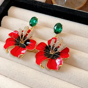Primo piano di orecchini a fiore in smalto rosso con gemme verdi e cristalli brillanti.