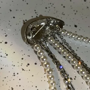 Close-up detail view of a jellyfish brooch with long pearl and rhinestone tassel chains