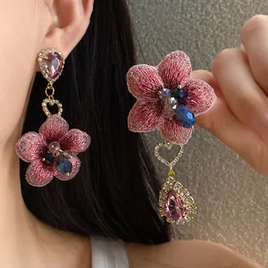Dettaglio di orecchini a fiore ricamati rosa con goccia di cristallo e cuore piccolo