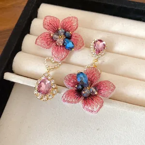 Dettaglio di orecchini asimmetrici a fiori rosa e gocce di strass su vassoio portagioielli