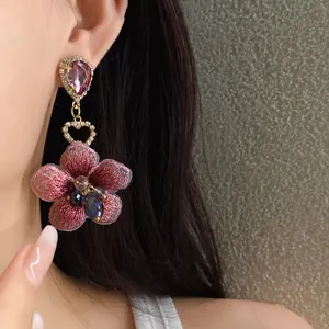 Dettaglio di orecchino a fiore ricamato rosa con strass e ago in argento, stile elegante.