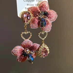 Dettaglio di orecchini floreali asimmetrici con pendenti in cristallo rosa a goccia