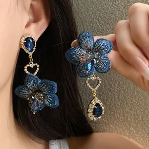 Dettaglio di orecchini a fiore blu asimmetrici con cristalli a cuore e a goccia
