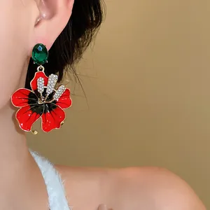 Primo piano di eleganti orecchini a forma di fiore rosso con cristallo verde e strass.