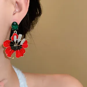 Dettaglio di eleganti orecchini a fiore rosso con pietre preziose verdi sul lobo
