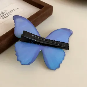 Close-up detail of the back of a blue butterfly hair clip showing its black duckbill fastener