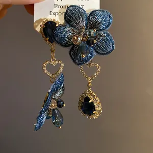 Primo piano degli orecchini asimmetrici di lusso con fiori blu e gocce di cristallo blu navy