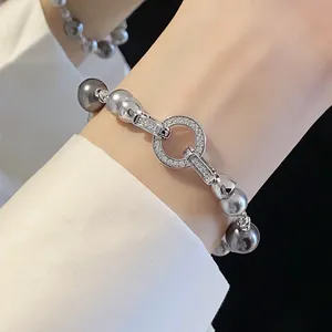 Dettaglio ravvicinato di un bracciale in argento con zirconi e perle grigie su un polso