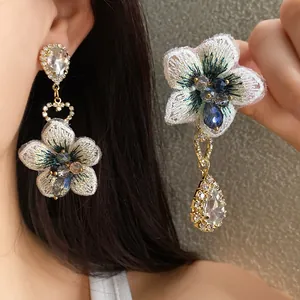 Dettaglio orecchini a fiore asimmetrici con ricami intricati e cristalli a goccia