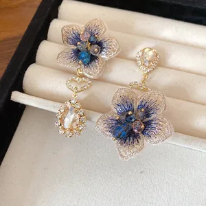 Macro dettaglio di orecchini a fiori asimmetrici con petali ricamati e cristalli