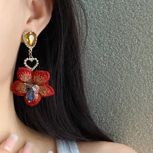 Primo piano di un orecchino a fiore rosso ricamato con strass e cristallo a goccia