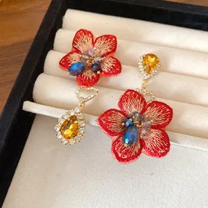 Dettaglio di orecchini asimmetrici a fiore rosso con gemme a goccia d'acqua gialle.