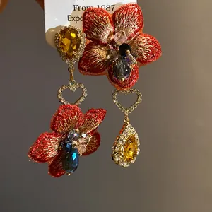Primo piano dettagliato di orecchini asimmetrici con fiori ricamati rossi e cristalli