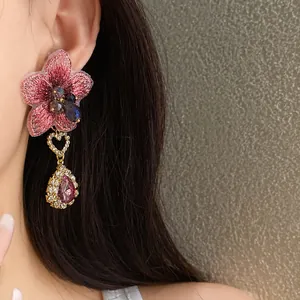 Dettaglio di orecchino asimmetrico con fiore ricamato rosa e goccia di cristallo.