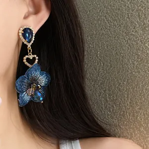 Primo piano dettagliato di un elegante orecchino a fiore blu e goccia d'acqua su orecchio