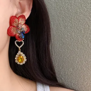 Primo piano di orecchini eleganti con fiore rosso ricamato e ciondolo a goccia giallo.