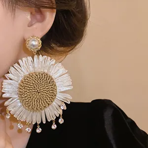 Detailansicht eines großen Boho-Gänseblümchen-Ohrrings aus Stroh mit Perlen an einem Model.