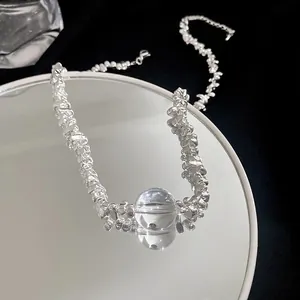 Detailed macro view of a silver baroque necklace with a clear glass bead pendant on a mirror
