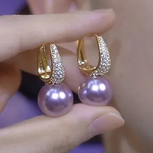Close-up of elegant gold hoop earrings featuring zircon pave and large purple pearls.