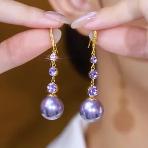 Close-up of elegant gold drop earrings with purple stones and pearls held by hand.