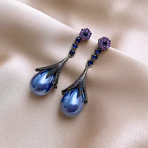 Macro detail of vintage-style blue pearl drop earrings with purple zircon floral accents