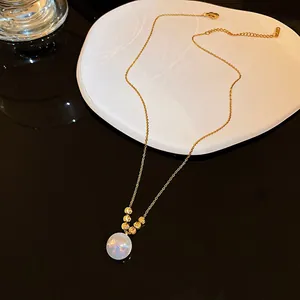 Detailed view of a gold chain necklace with iridescent white pendant and gold beads