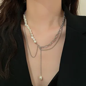 Macro detail of a baroque pearl and silver link chain layered necklace on a model.