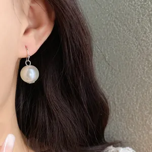 Close-up of elegant large pearl drop earring with silver hook on model with dark hair