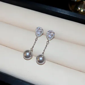Close-up of elegant drop earrings with pear-shaped zircon and grey pearls in a jewelry box.