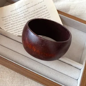 Gros plan détaillé d'un jonc en résine marron foncé vintage dans un plateau à bijoux beige chic.