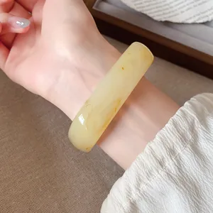 Gros plan d'un bracelet jonc irrégulier en résine jaune crème de style rétro sur un poignet