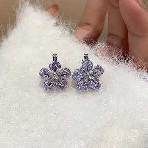Macro detail of sparkling purple zirconia flower earrings on a white soft fluffy fabric