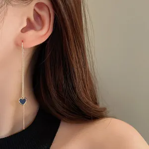 Detailansicht eines langen Quastenohrrings mit elegantem blauem Herzanhänger an einem Model.
