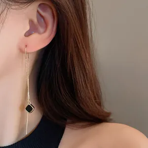 Detailansicht eines eleganten langen goldenen Quastenohrrings mit schwarzem Quadrat