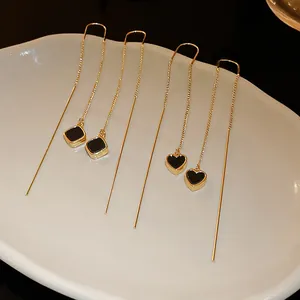 Detailaufnahme goldener Durchziehohrringe mit schwarzen Herz- und Quadrathängern