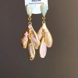 Dettaglio di orecchini dorati stile retrò con pennellate di smalto rosa e azzurro