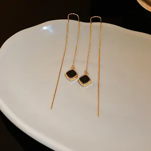 Detailansicht von Gold-Quastenohrringen mit schwarzem geometrischem Anhänger