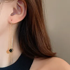 Nahaufnahme einer eleganten goldenen Quasten-Ohrlinie mit schwarzem quadratischem Anhänger.