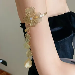 Close-up of elegant gold floral arm cuff with zircon and dangling leaf tassels.