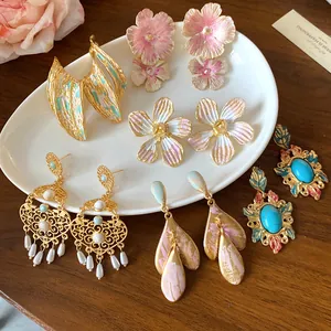 Selezione di orecchini vintage a fiore in smalto e placcati oro su un piatto di ceramica.