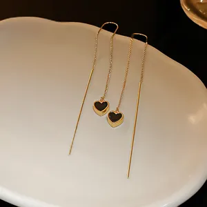 Detailansicht eleganter goldener Quastenohrringe mit minimalistischen schwarzen Herzanhängern