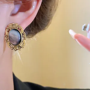 Close-up of a vintage oval resin stud earring with an antique gold-tone frame on an ear.