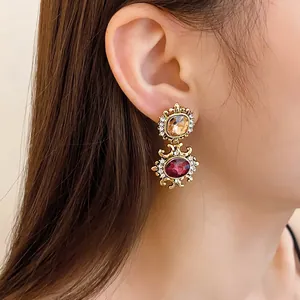 Close-up of vintage palace style drop earrings with amber and ruby red crystals on model